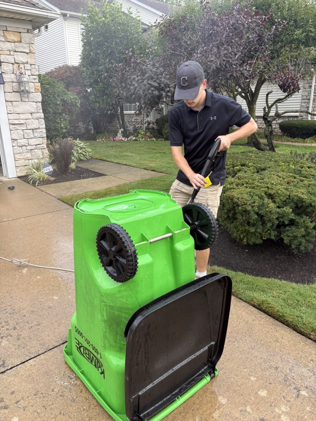 Pressure washing a trash bin on a residential driveway