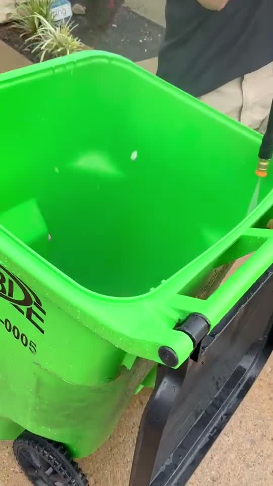 Rinsing a freshly cleaned green trash bin exterior
